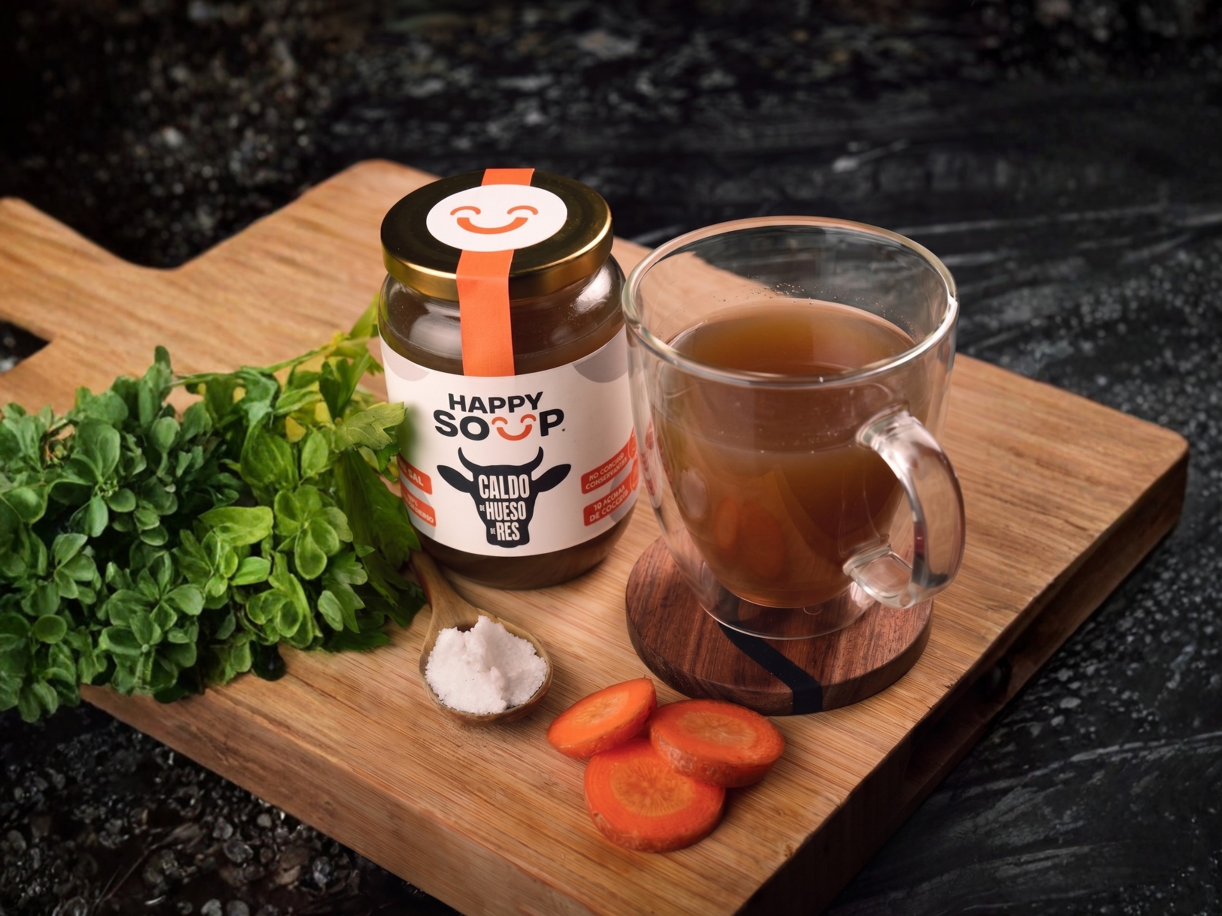 Caldo de hueso Happy Soup servido sobre tabla de madera con ingredientes